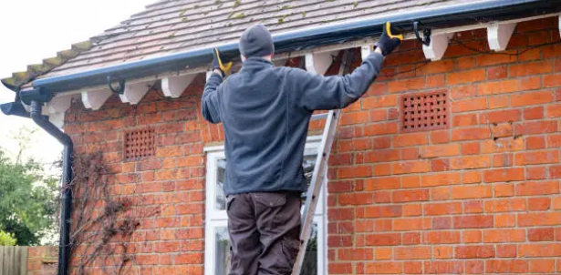 Gutter cleaner on a ladder clearing leaves from the fascia of a brick Sydney home